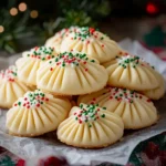 Christmas Whipped Shortbread Cookies topped with holiday sprinkles and maraschino cherries, arranged on a festive table.