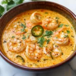 A bowl of creamy spicy jalapeño shrimp soup garnished with fresh cilantro and served with lime wedges on the side.