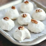 A plate of glossy, snowy-white Easy Divinity Candy pieces topped with chopped pecans, perfect for holiday gifting.