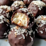 Close-up of No-Bake Coconut Cream Balls, coated in chocolate, placed on parchment paper with a sprinkle of shredded coconut on top.