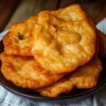 Golden brown Indian Frybread served with honey and powdered sugar on a rustic plate.