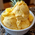 A scoop of homemade pineapple ice cream in a bowl, topped with toasted coconut and mint.