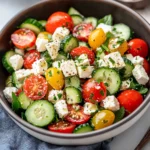 Greek cucumber tomato salad with crumbled feta, olives, and fresh herbs in a white bowl