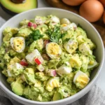 A bowl of creamy avocado egg salad garnished with herbs