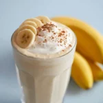 A glass of creamy banana breakfast smoothie topped with a sprinkle of cinnamon and served with a reusable straw.