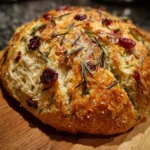 Crusty no-knead rosemary cranberry bread brushed with olive oil and topped with flaky sea salt